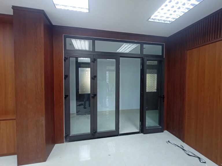 Lối vào cửa kính khung nhôm, tường ốp gỗ hai bên – phòng truyền thống Công an quận Hải Châu, Đà Nẵng